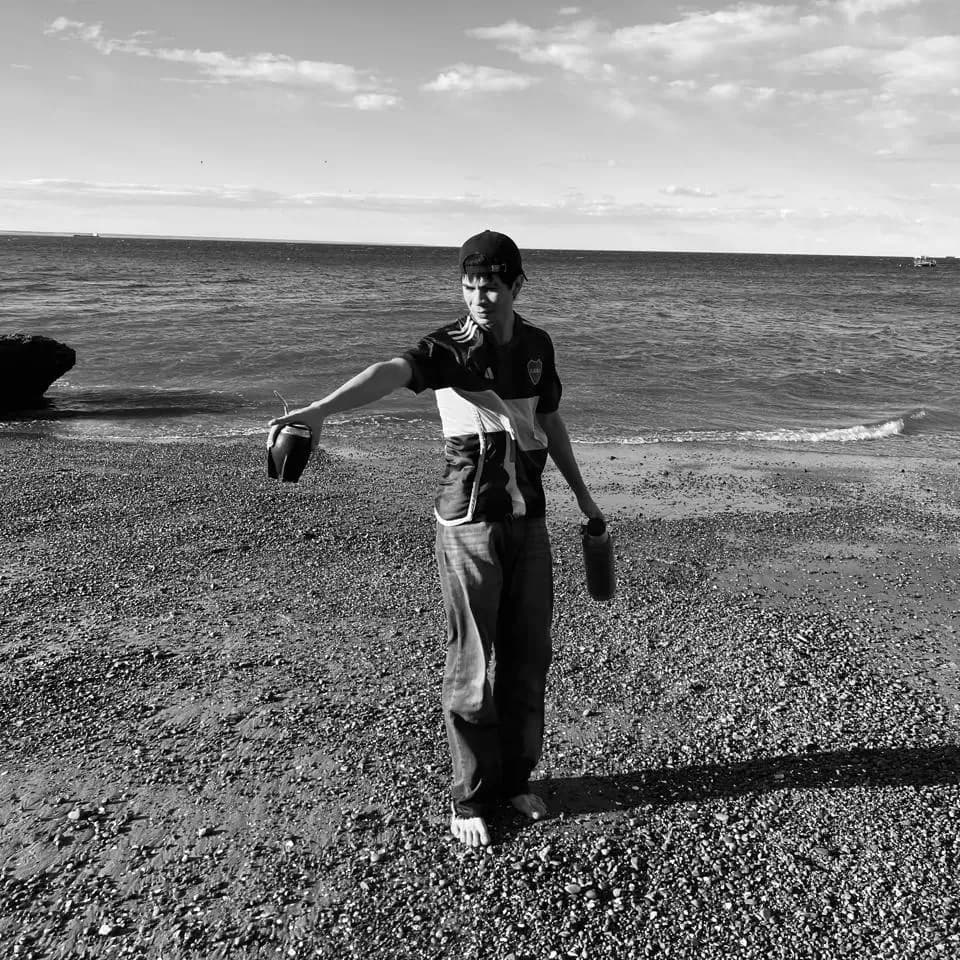A black and white image at the beach with a Boca jersey and mate.